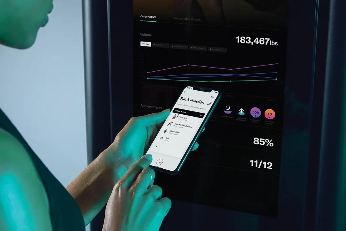 Phone showing a custom workout builder in front of a Tonal smart home gym screen